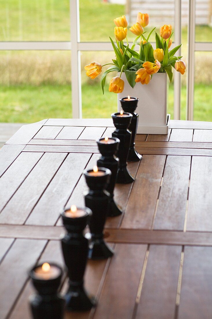 Row of candlesticks and bouquet of tulips on wooden table
