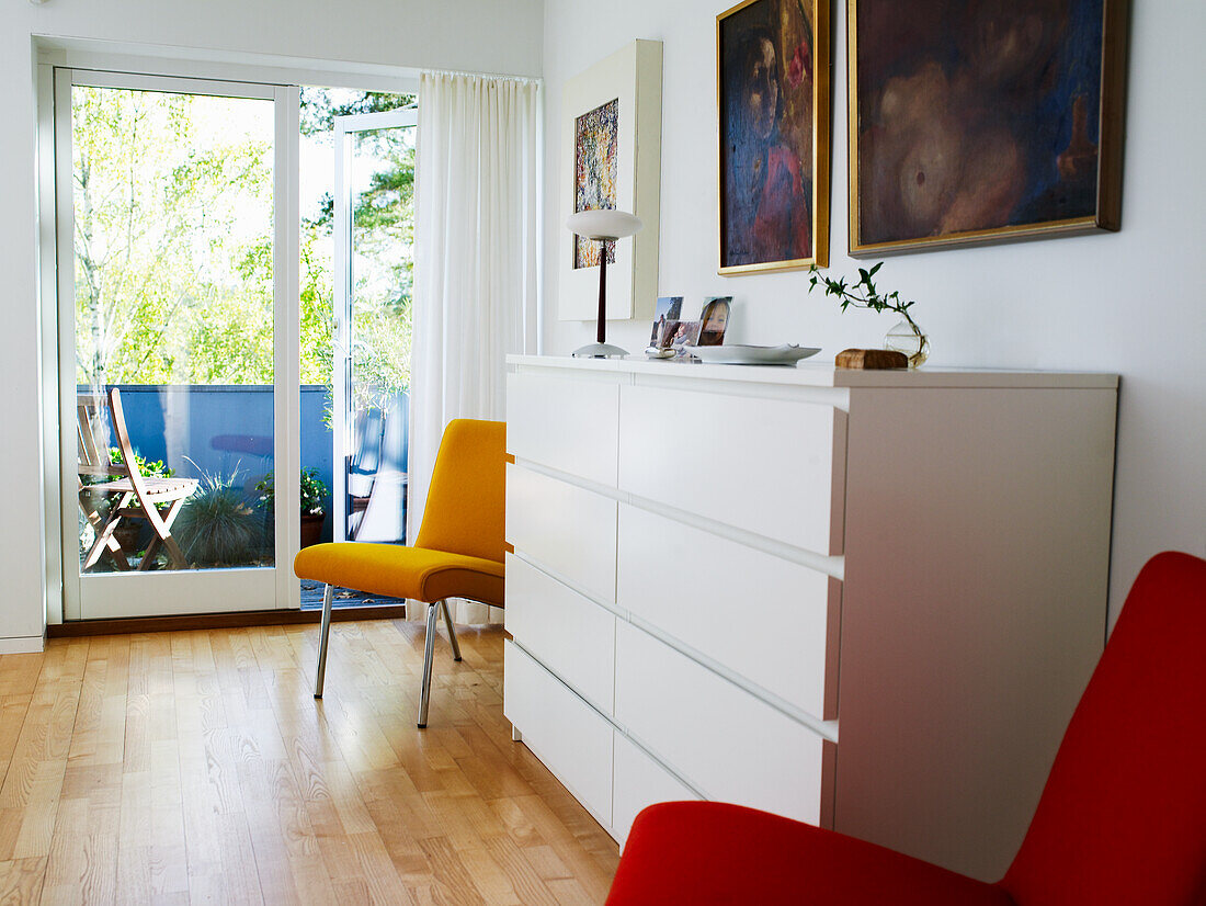 Brightly lit room with red chair and yellow chair next to white chest of drawers