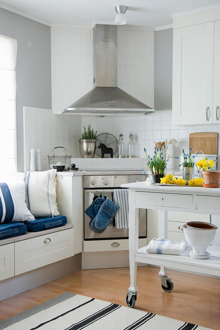 Small kitchen in white with mobile cart and bench by the window