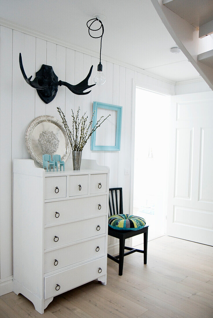 White chest of drawers with decoration and chair in a light-colored hallway