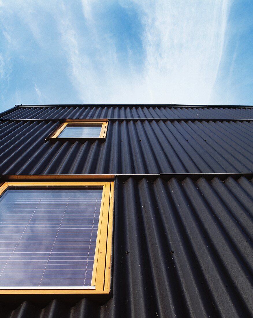 House facade with black corrugated metal cladding and light wooden windows