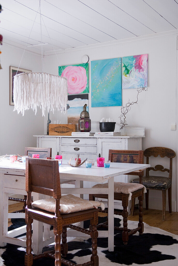 Country-style dining area with white wooden table and colorful paintings