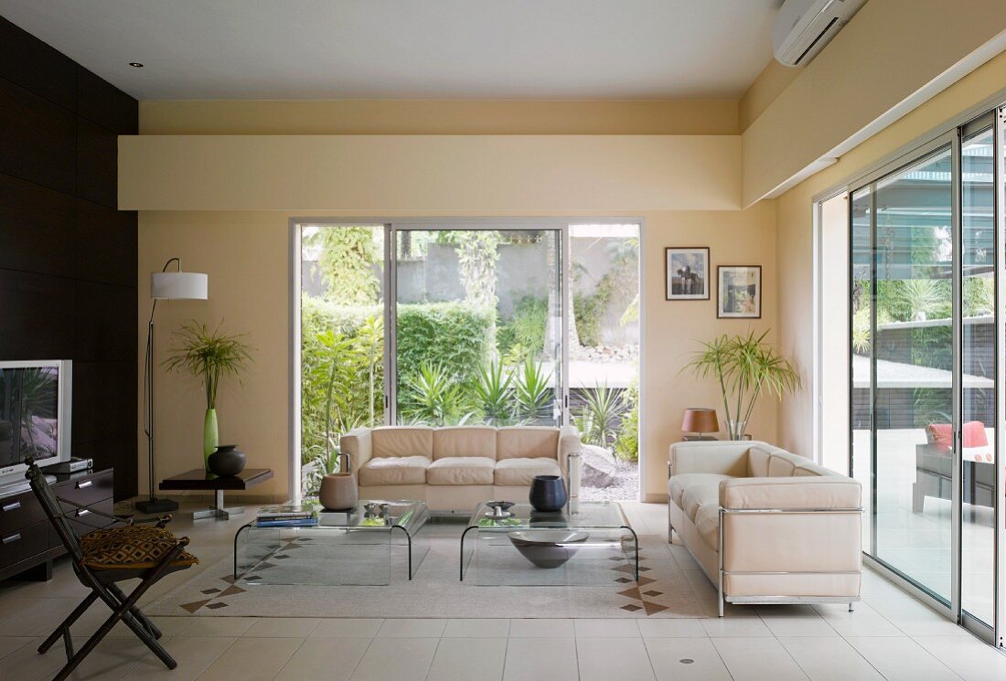Wohnzimmer mit cremefarbenen Sofas im Bauhausstil vor grossen Schiebefenstern