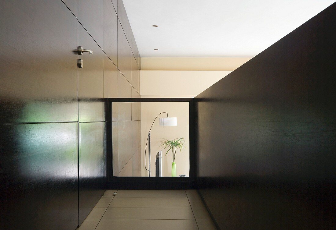 Galeriegang mit in dunkle Holzverkleidung integrierter Zimmertür und Glasbrüstung mit Blick in tieferliegendes Wohnzimmer