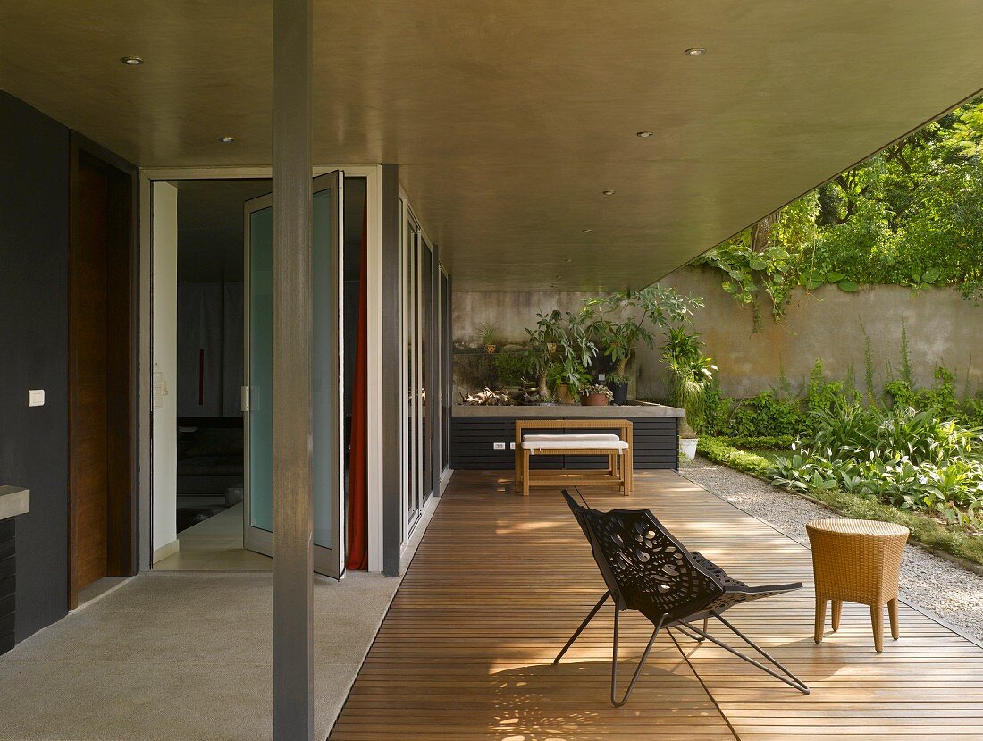 Metallsessel mit schalenförmiger Stoffbespannung und Beistelltisch auf betonüberdachter Terrasse mit Holzdeck
