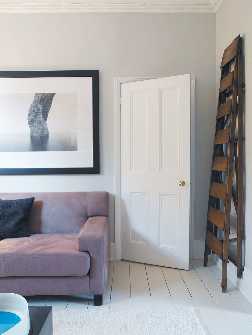 Ein Sofa unter einem Bild und eine Leiter neben der Tür in einem Wohnzimmer