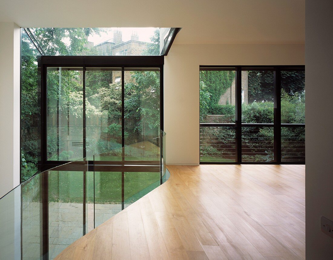 View of garden through modern, glass foyer with gallery level