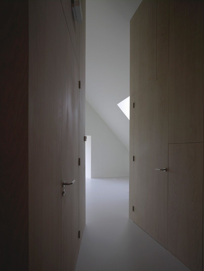 Room with sloping attic ceiling at end of narrow, tapering corridor with integrated doors flush with wood cladding