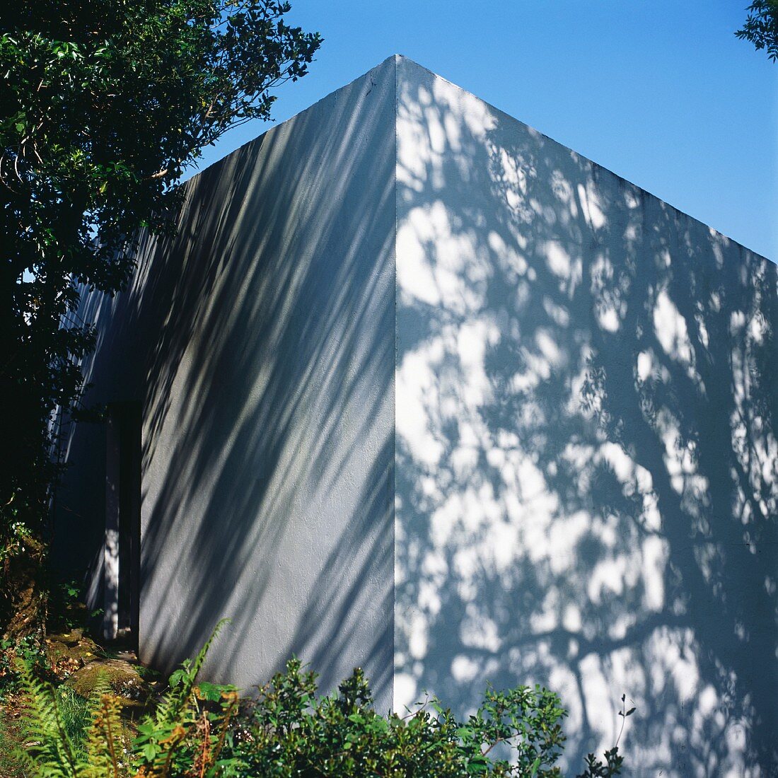 White, cubic building embedded in landscape with patterns of light and shade