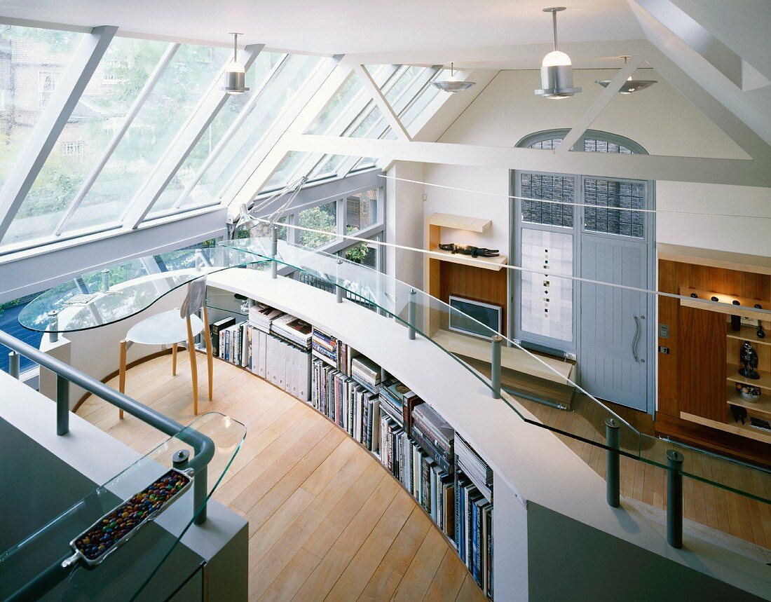 Open-plan, double-height living space - office with teardrop-shaped glass desk and curved storage in gallery balustrade