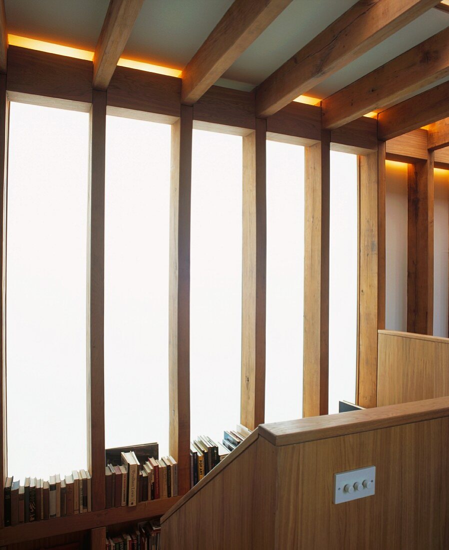 Volle Bücherregale vor Milchglas Fensterstreifen im Treppenaufgang eines Holzhauses mit sichtbarer Tragkonstruktion