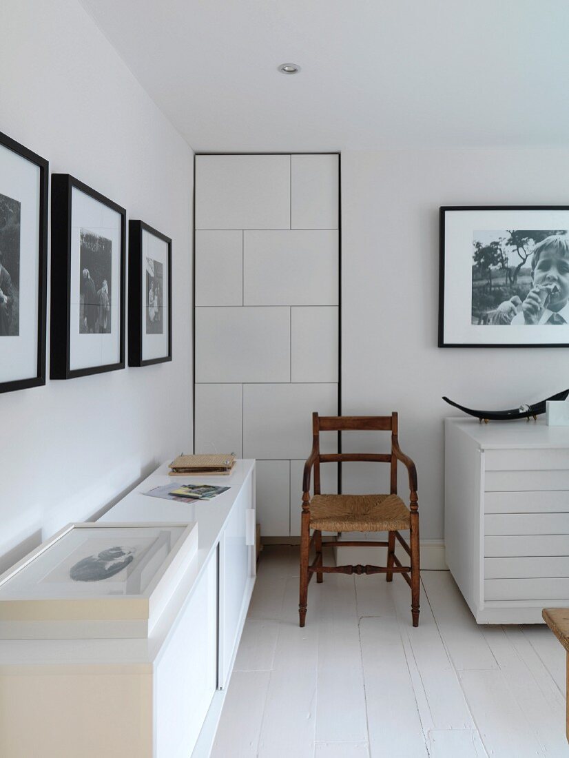 Weisses Zimmer mit einem Sideboard, einem alten Stuhl und schwarz-weiss Fotos an den Wänden