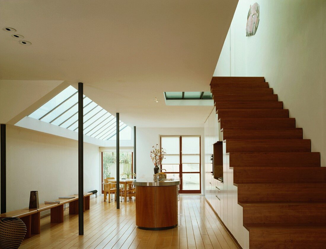 Open-plan living space with kitchen, benches, dining table & wooden staircase