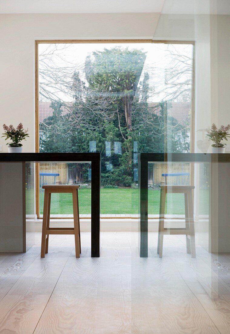 Reflection of counter with bar stool in front of panoramic window with view of garden
