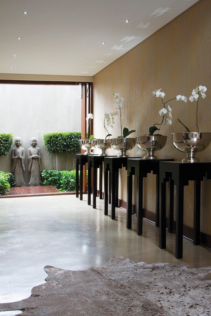 Halle mit weissen Orchideen in reflektierenden Silberschalen auf schwarzen Sockeln im chinesischen Stil