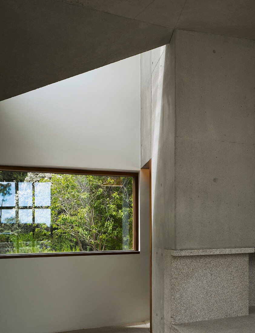 Innenraum aus grauem Sichtbeton mit Fenster und Blick auf Grün