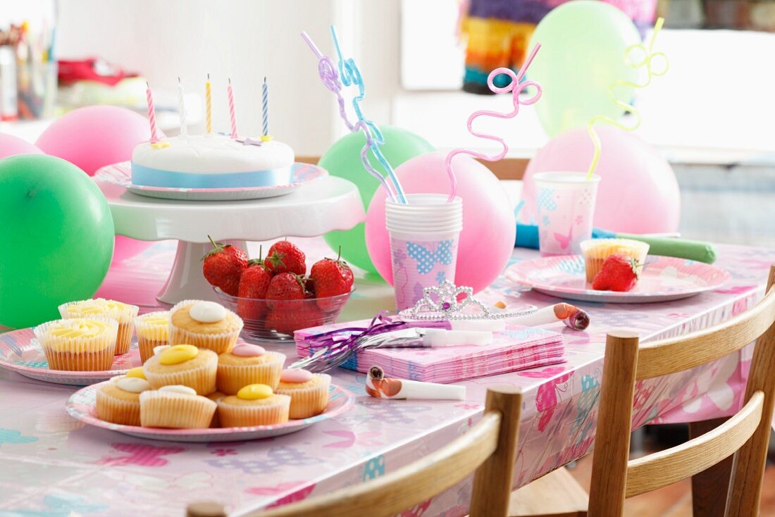 Rührteiggebäck, frische Erdbeeren und Geburtstagstorte für Kinder auf einem Tisch mit Partydeko