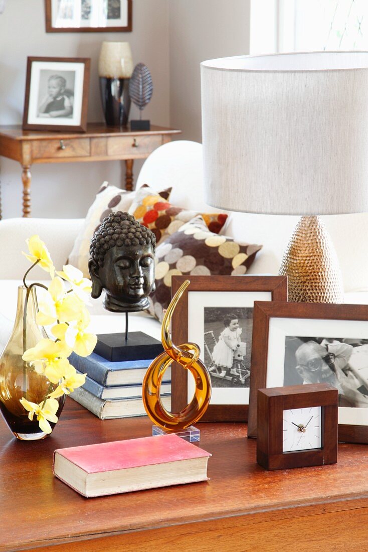 Side table with alarm clock, books, orchid, Buddha's head, table lamp and black and white photograph