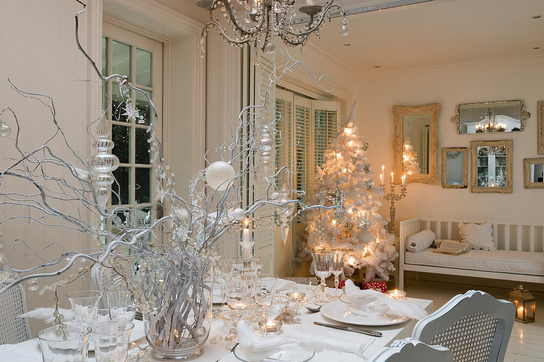 Festlich gedeckter Esstisch vor beleuchtetem Christbaum in weißem Wohn- und Esszimmer