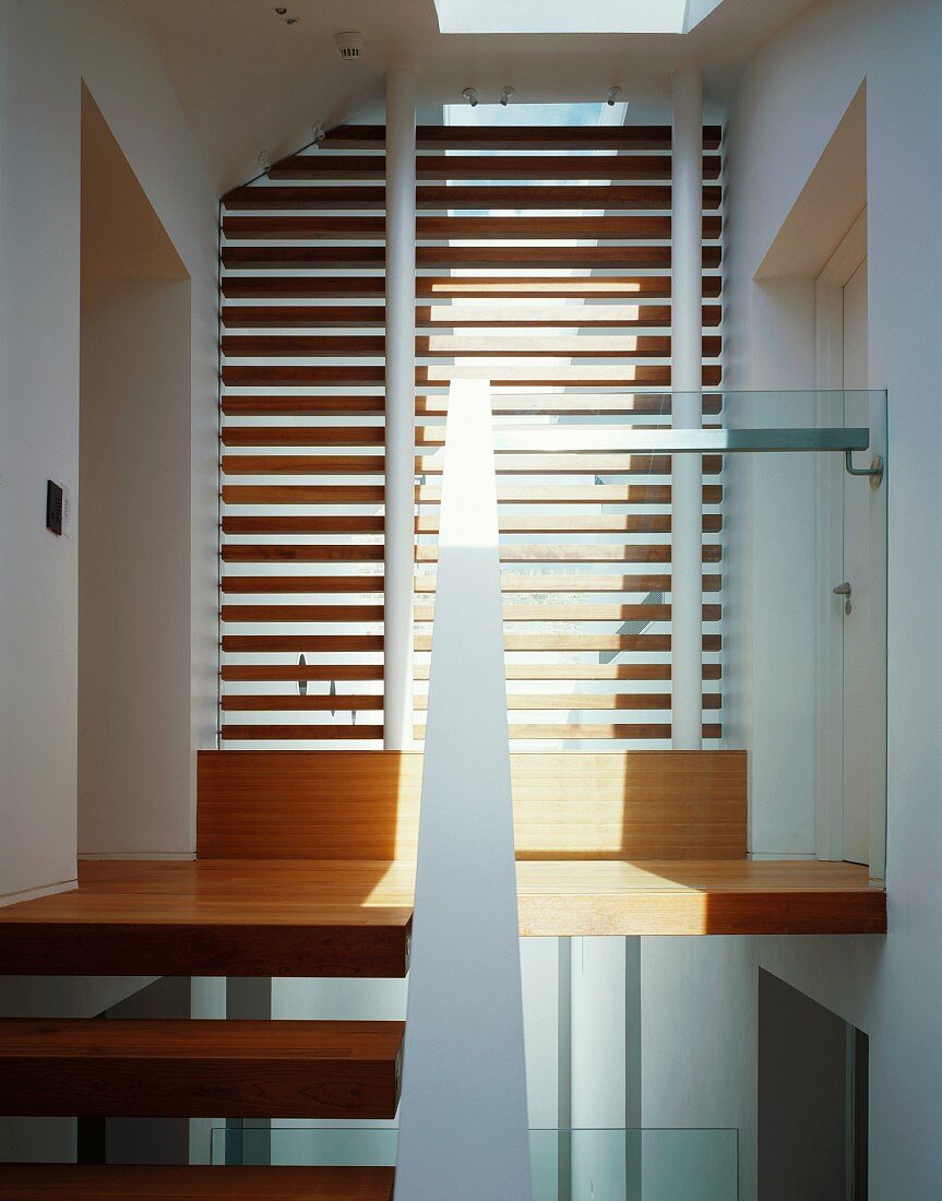 Lamellen vor raumhohem Fenster und Treppenstufen aus Holz im modernen Treppenhaus