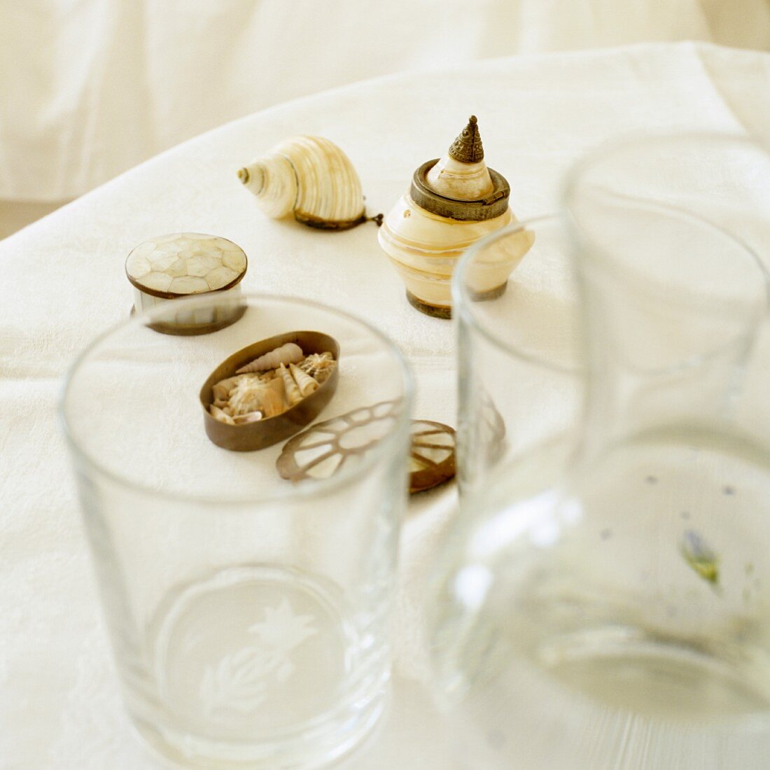 Trinkgläser und verschiedene Muschelgehäuse auf weisser Tischdecke