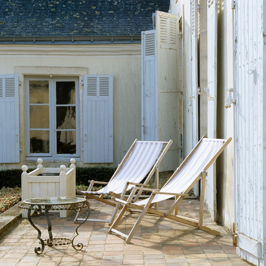 Liegestühle aus Holz auf sonnigem Terrassenplatz vor mediterranem Haus