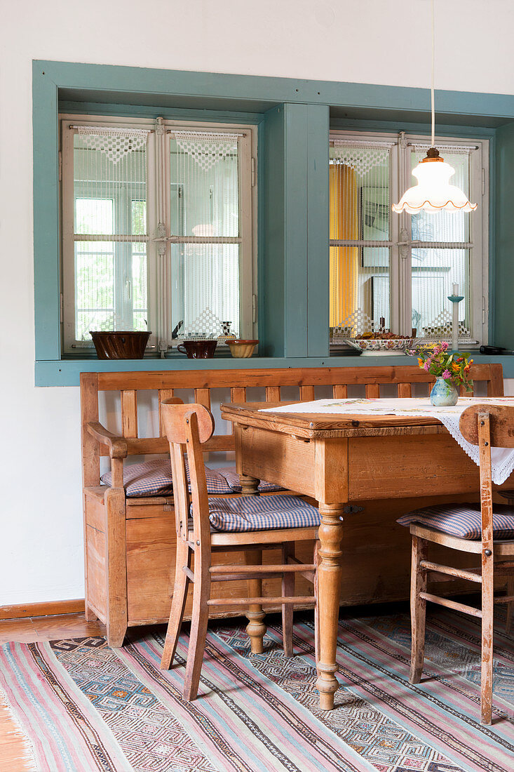 Esstisch mit Stühlen und Sitzbank aus hellem Holz an Fenster einer Loggia und Vintage Hängeleuchte