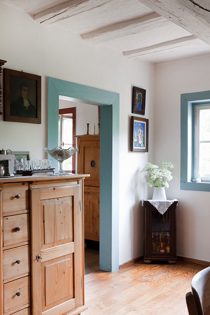 Half-height rustic cabinet with drawers next to open doorway with frame painted pale blue in farmhouse