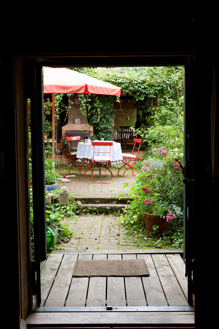 Blick durch offene Haustür in Garten auf rote Gartenstühle unter dem Sonnenschirm