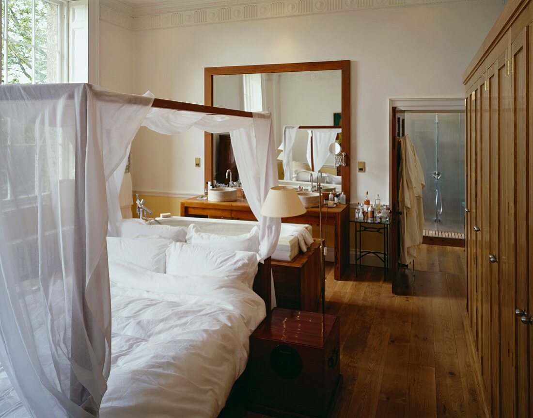 Himmelbett mit weißem Vorhang vor Badewanne und Waschbereich im Schlafzimmer