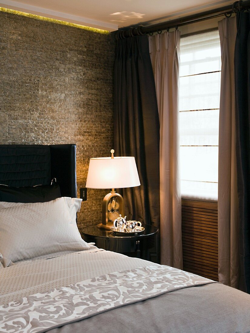 Schlafzimmerecke - Nachttisch mit Lampe neben Bett und teils geschlossenem Vorhang am Fenster