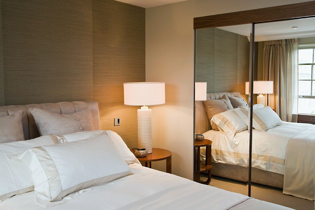 Schlafzimmerecke mit Nachttisch und Lampe neben eingebautem Spiegelschrank