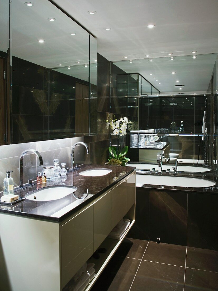 Designer bathroom with two sinks in washstand and black-tiled walls and bathtub