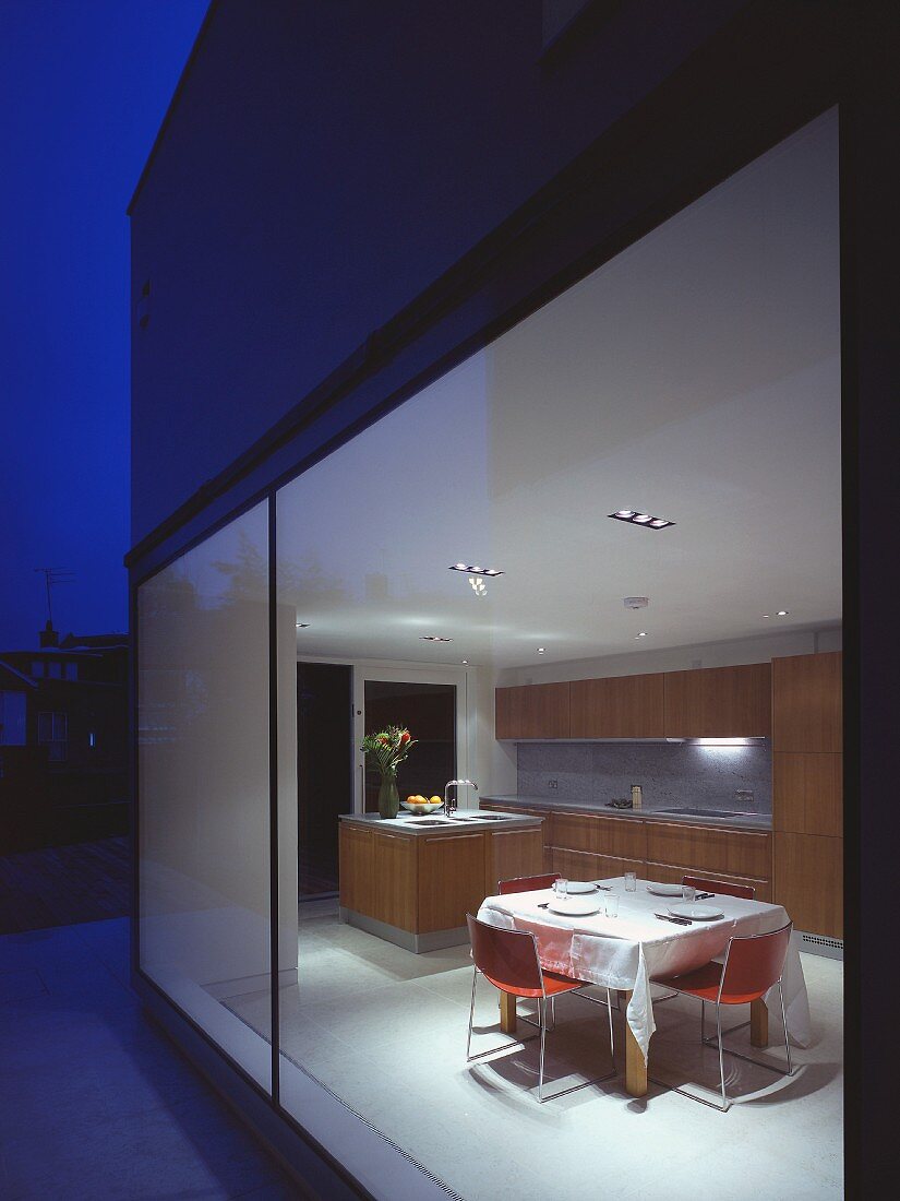 Modernes Wohnhaus in Nachtstimmung mit Blick in beleuchtete Küche auf Essplatz