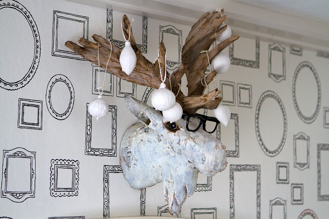 Wooden antler decoration with glasses and white baubles on wall with picture frame wallpaper