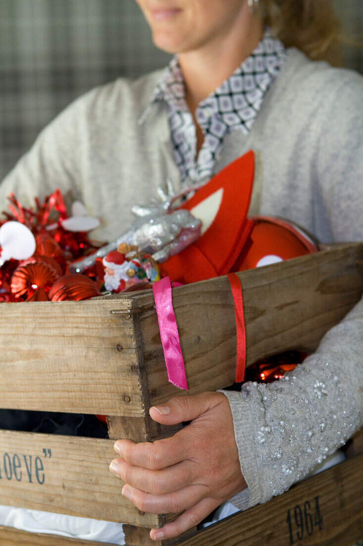 Person hält eine Holzkiste mit Weihnachtsdeko