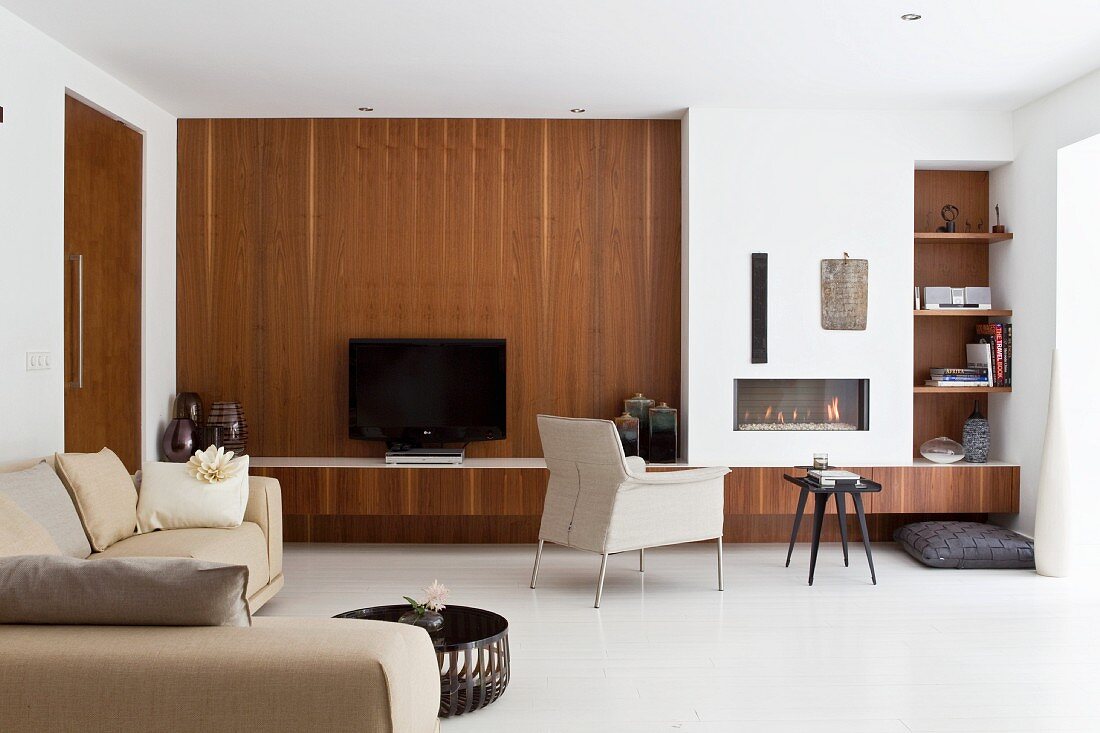 Modern living room with dark wood cladding on wall next to integrated fireplace