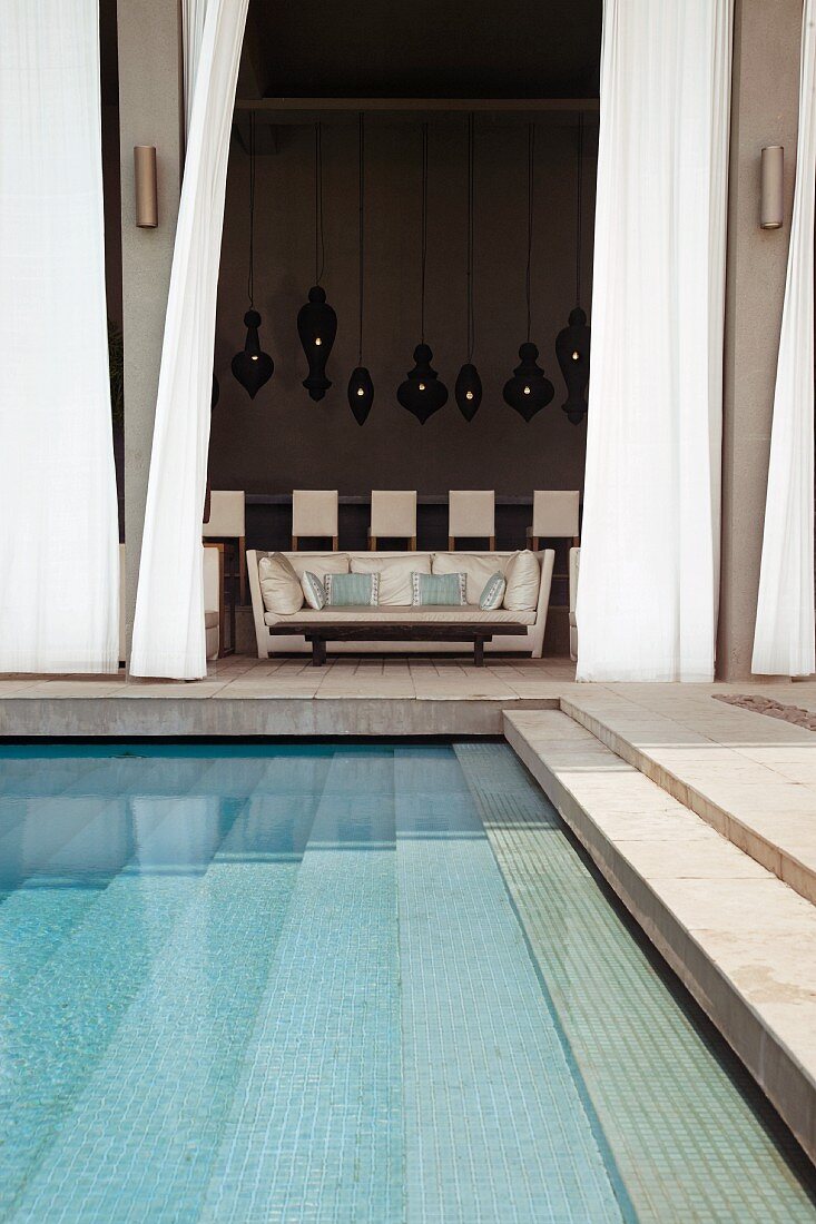 Terrasse mit Stufenanlage im Pool und Blick durch offenen Vorhang auf elegantes Sofa