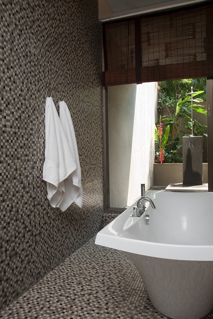 Freistehende Badewanne und Mosaikfliesen auf Wand und Boden in modernem Bad mit offenem Durchgang zum Innenhof