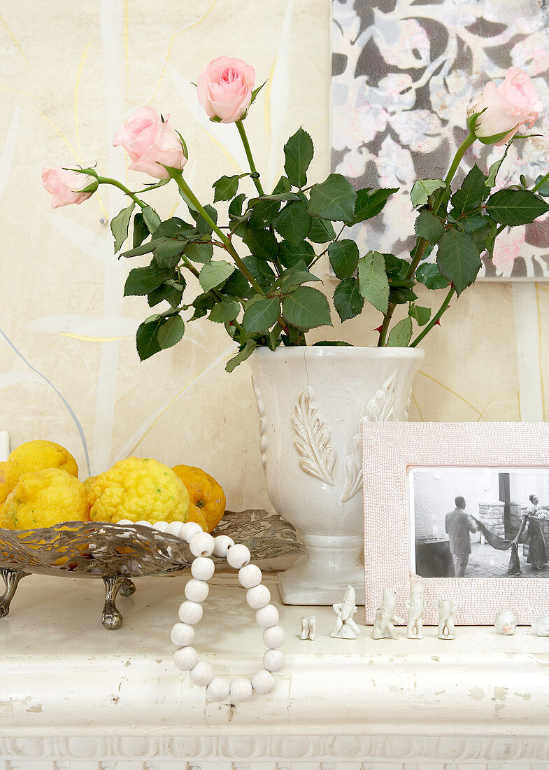 Dish of lemons next to roses in white vase
