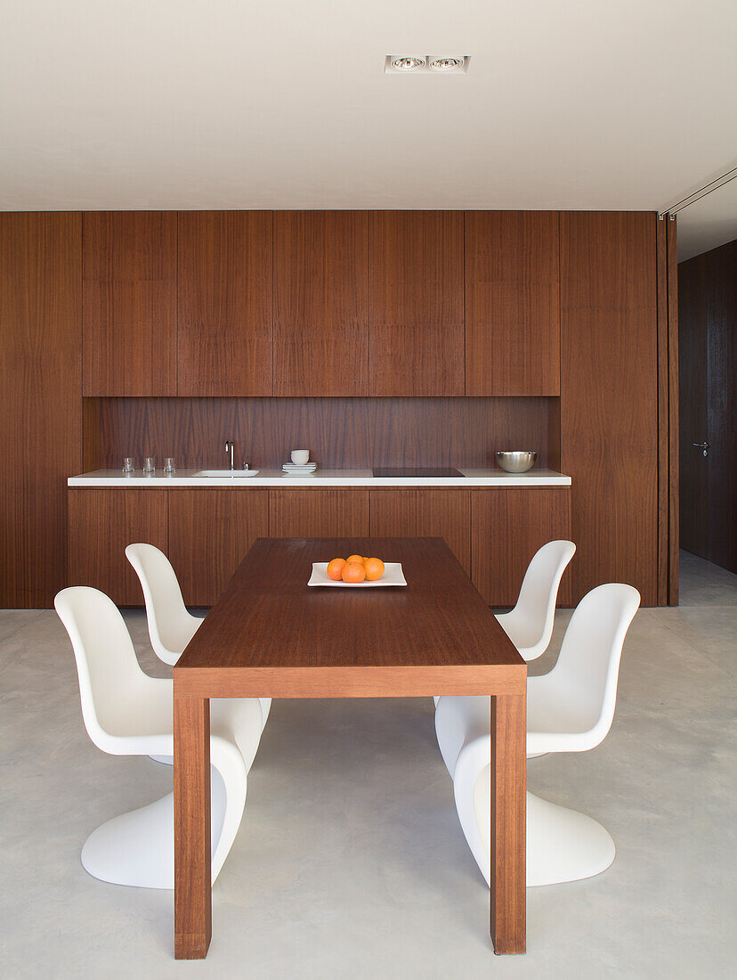 Holztisch mit weißen Stühlen vor paneelartiger Wandverkleidung im Esszimmer