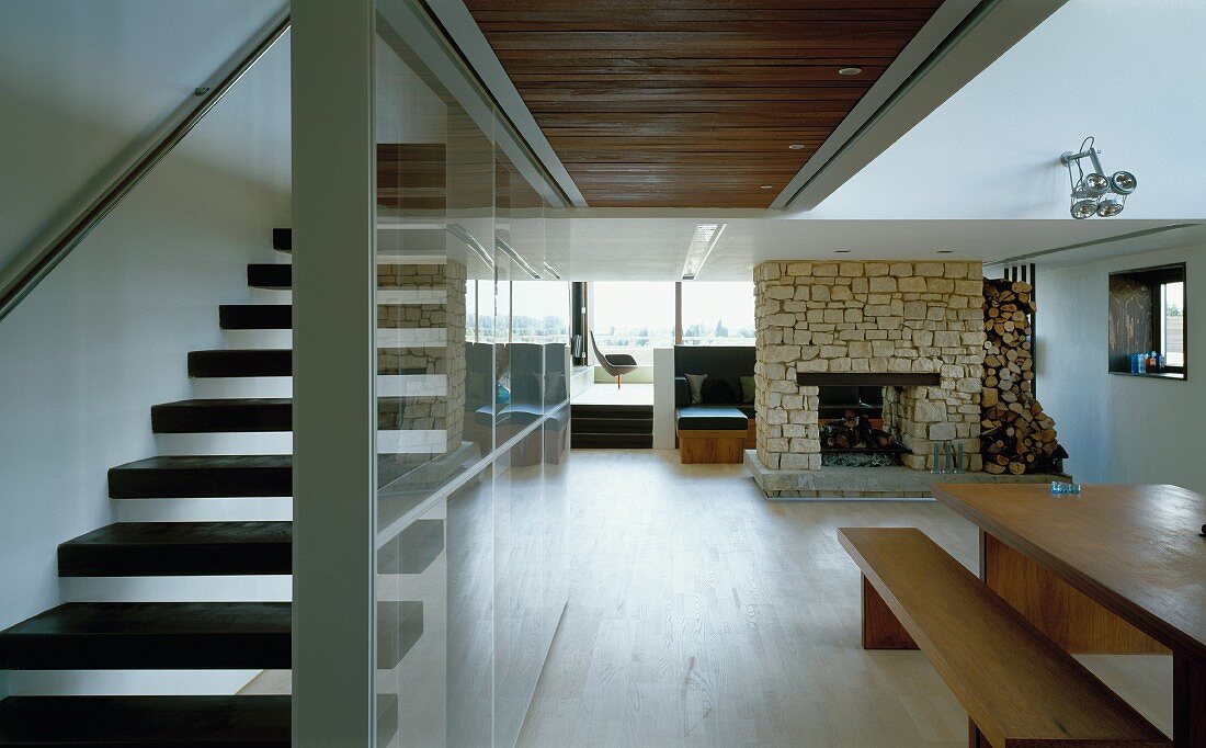 Open-plan living space with dining table, fireplace and staircase separated by glass wall
