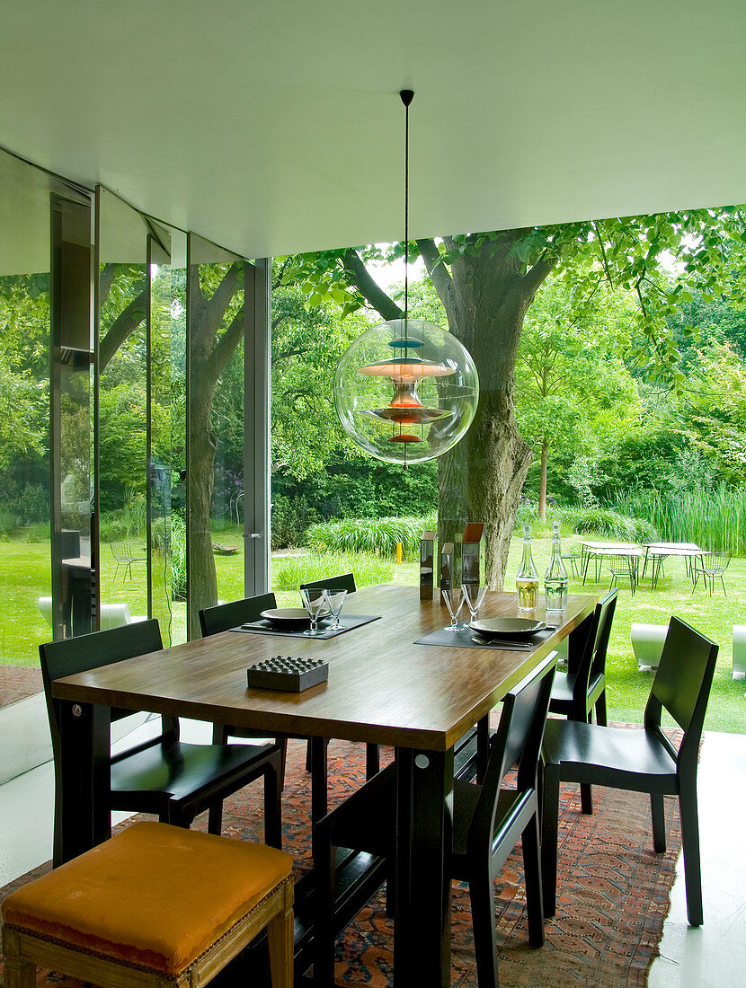 Eleganter Tisch und Stühle aus dunklem Holz und Bauhaushängelampe auf der Terrasse mit Gartenblick
