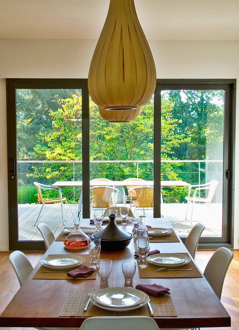 Ballonartige Hängelampen aus Holzstreifen über gedecktem Tisch vor Terrassentür mit Gartenblick