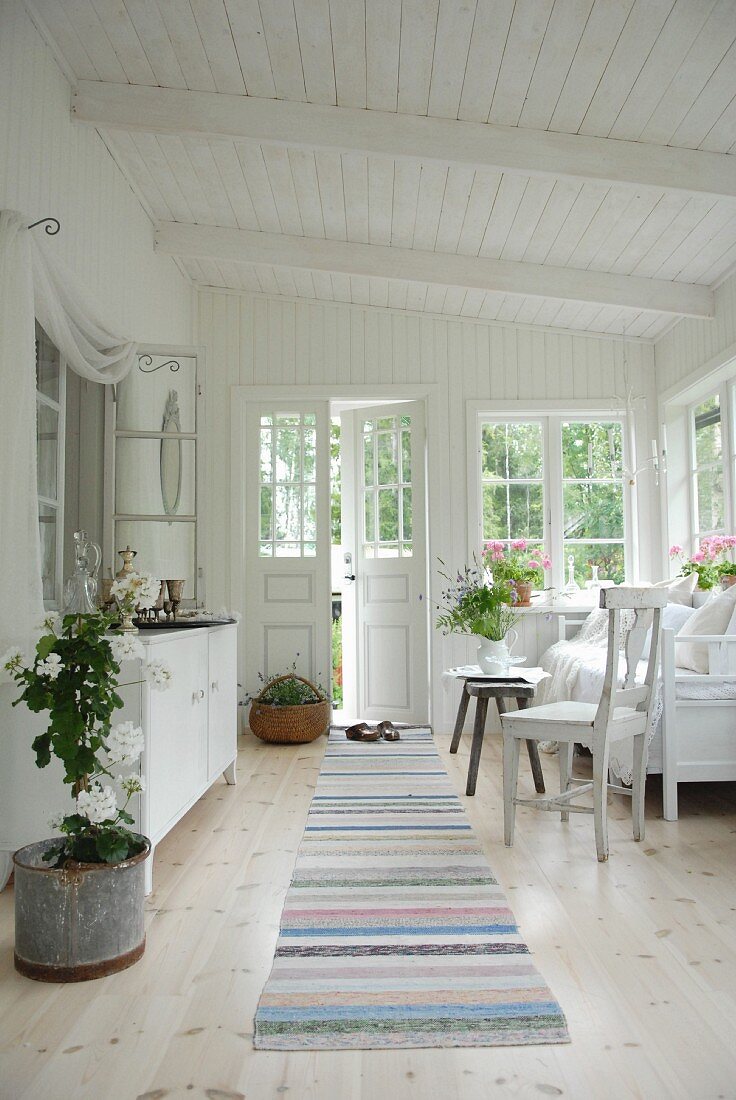 Loggia of white wooden house with white furniture and striped runner on wooden floor