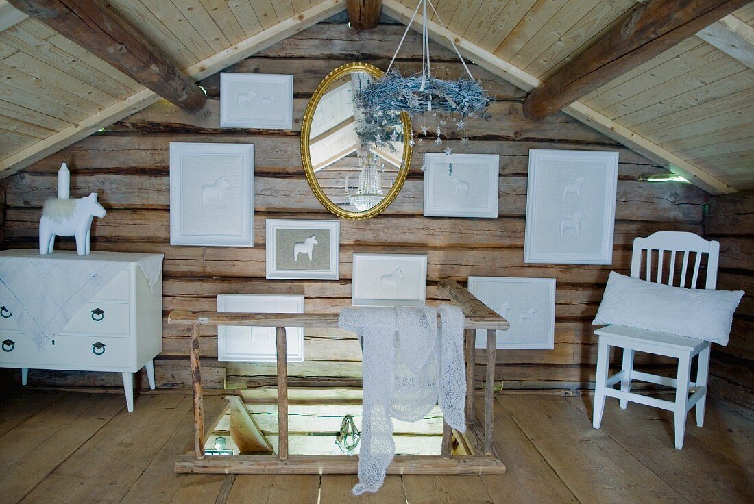 Dachgeschoss eines Holzhauses mit aufgehängten Bildern an Holzwand und Ausstieg einer Treppe mit schlichtem Holzgeländer