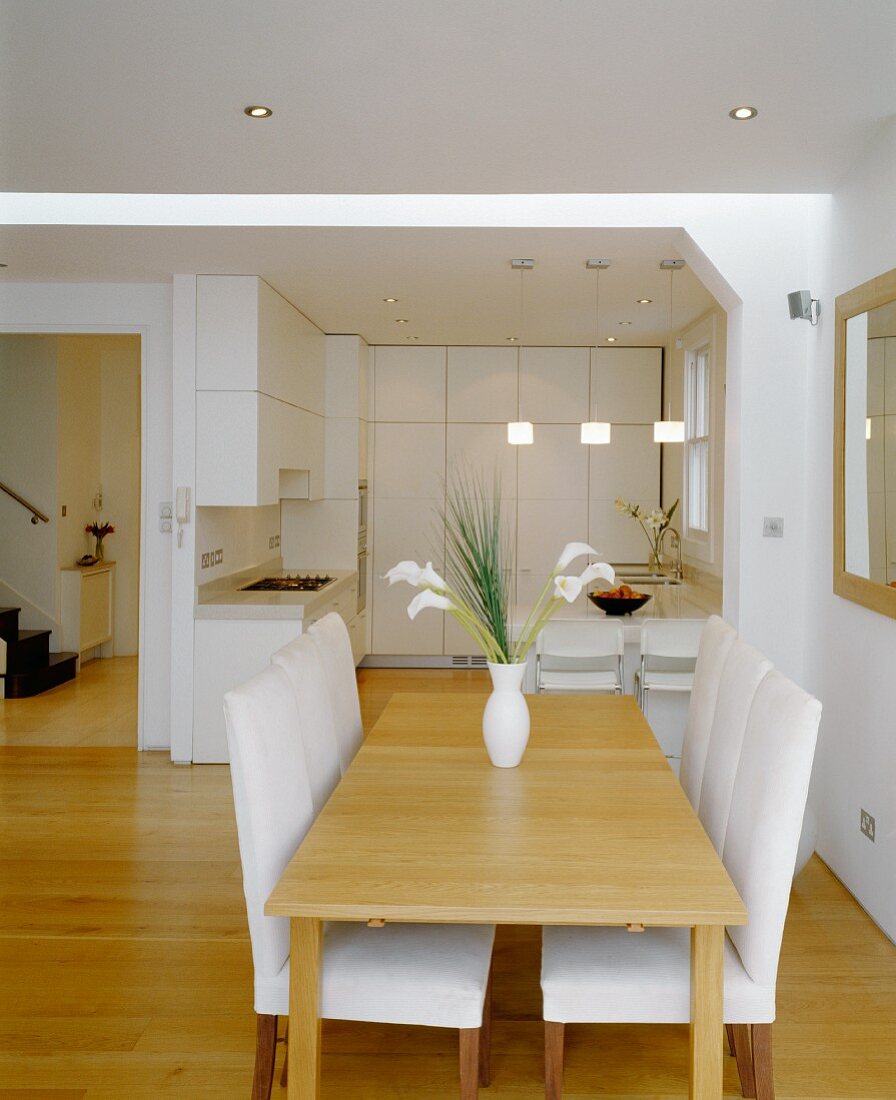 Esstisch aus Holz und gepolsterte Stühle mit weißem Bezug im offenen Wohnraum