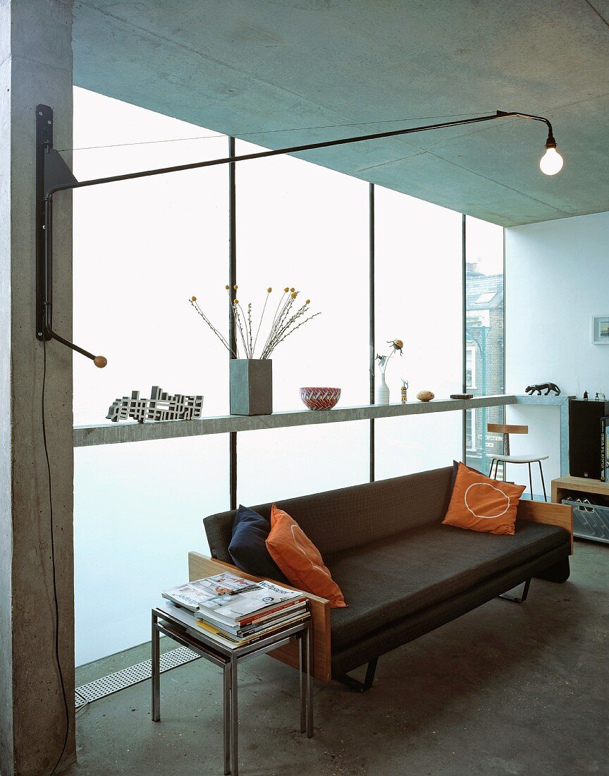 Wandleuchte mit schwenkbarem Kragarm und schwarze Ledercouch vor opaker Fensterfront im zeitgenössischen Wohnraum