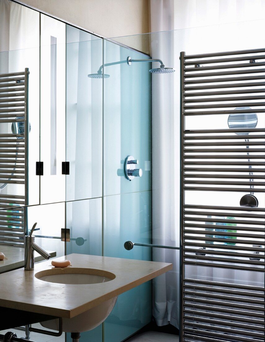 Small designer bathroom with washstand next to glass shower partition and stainless steel, heated towel rail