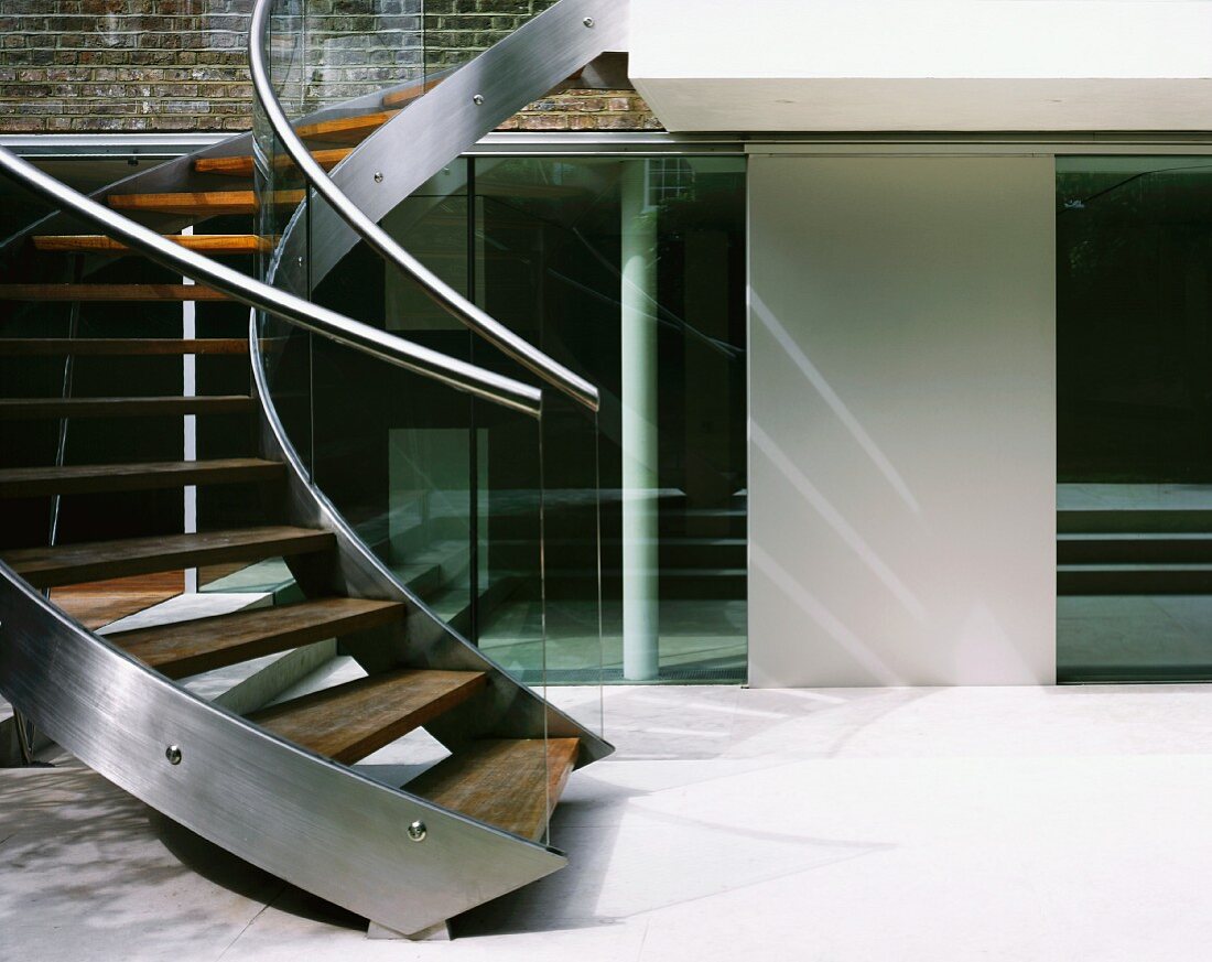 Curved staircase with stainless steel stringer and wooden treads in courtyard of contemporary house